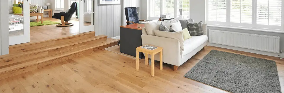 A modern living room with professionally installed laminate flooring, a beige sofa, a small side table, a gray rug, and large windows with white shutters in Colorado Springs, CO